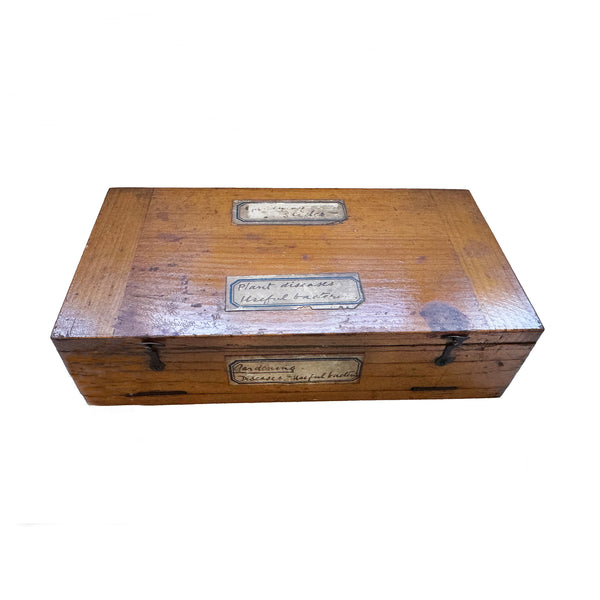 A closed wooden box with labels and hinges with microscope slides inside