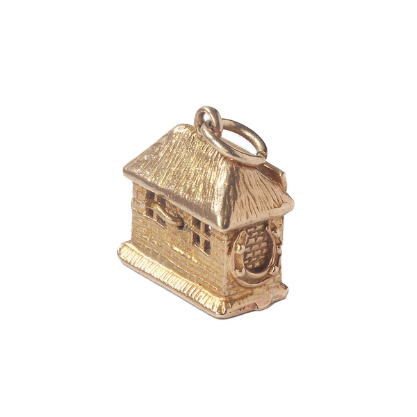 A vintage gold charm with blacksmith inside a house horseshoes each side